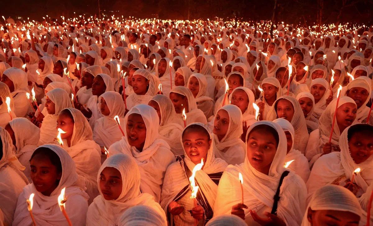 Ethiopian Orthodox worshippers in white netela shawls holding candles during the Fasika midnight vigil